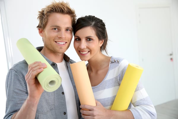 Portrait of smiling couple holding wallpaper rolls